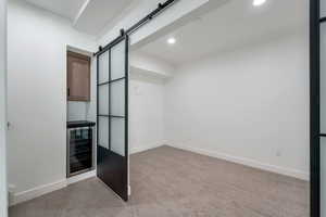 Unfurnished bedroom featuring a barn door, beverage cooler, light carpet, and recessed lighting