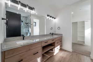 Full bathroom with a stall shower, double vanity, a spacious closet, and light wood-style floors