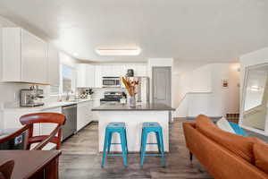 Kitchen with white cabinetry, dark wood-style floors, appliances with stainless steel finishes, a center island, and open floor plan
