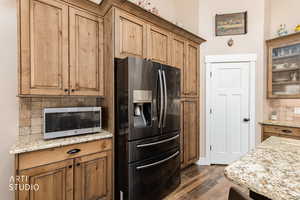 Kitchen with tasteful backsplash, black refrigerator with ice dispenser, light stone countertops, and dark wood finished floors