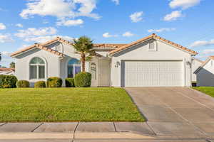 Mediterranean / spanish home with stucco siding, an attached garage, driveway, and a front lawn