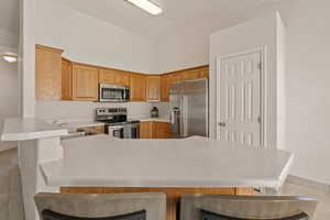 Kitchen with a kitchen bar, appliances with stainless steel finishes, a peninsula, light countertops, and vaulted ceiling