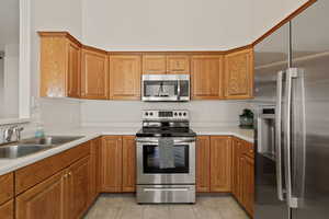 Kitchen featuring stainless steel appliances, light countertops, brown cabinetry, and light tile patterned floors