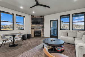 Living room with wood finished floors, a stone fireplace, ceiling fan, and recessed lighting