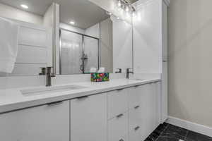 Full bath with double vanity, a shower stall, and dark marble finish flooring