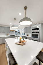 Kitchen featuring a kitchen bar, gray cabinetry, light wood finished floors, light stone countertops, and recessed lighting