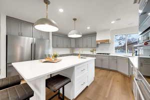 Kitchen featuring gray cabinets, stainless steel appliances, a kitchen bar, light wood-type flooring, and decorative light fixtures