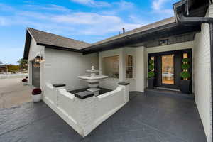 Entrance to property with brick siding, roof with shingles, an attached garage, and a patio