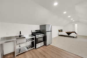 Kitchen featuring gas stove, recessed lighting, lofted ceiling, light wood-type flooring, and light colored carpet