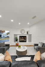 Living room featuring a decorative wall, recessed lighting, a premium fireplace, and wood finished floors