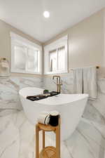 Bathroom featuring marble tiled flooring, a wainscoted wall, tile walls, a freestanding tub, and plenty of natural light
