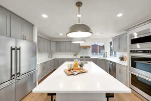 Kitchen featuring gray cabinets, appliances with stainless steel finishes, an island with sink, a breakfast bar area, and recessed lighting