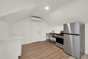Kitchen with appliances with stainless steel finishes, light wood-style floors, white cabinets, vaulted ceiling, and a wall mounted AC