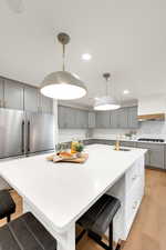 Kitchen featuring gray cabinetry, a breakfast bar area, light wood finished floors, decorative light fixtures, and recessed lighting