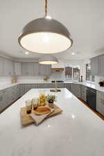 Kitchen featuring gray cabinets, light stone counters, dishwasher, recessed lighting, and decorative light fixtures