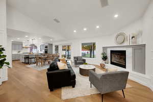 Living area featuring recessed lighting, light wood-style flooring, vaulted ceiling, a fireplace, and a decorative wall