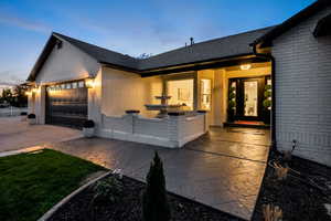 View of front of house with brick siding, an attached garage, a shingled roof, driveway, and covered porch