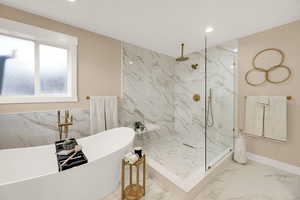 Bathroom featuring marble tiled floors, a freestanding tub, a marble finish shower, and recessed lighting