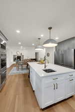 Kitchen featuring appliances with stainless steel finishes, light wood finished floors, an island with sink, light stone countertops, and pendant lighting