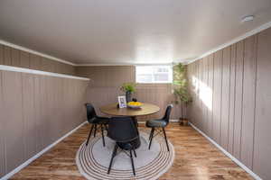 Dining area featuring light wood-style floors, wooden walls, and crown molding