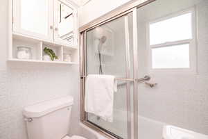 Full bathroom featuring combined bath / shower with glass door and tile walls