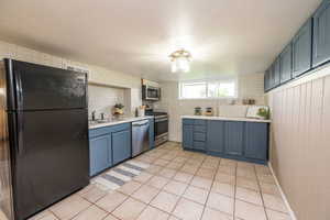 Kitchen with appliances with stainless steel finishes, blue cabinets, light countertops, light tile patterned floors, and decorative backsplash