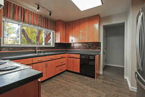 Kitchen featuring dark countertops, freestanding refrigerator, black dishwasher, decorative backsplash, and dark wood finished floors