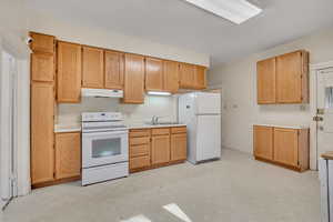 Kitchen featuring light floors, white appliances, light countertops, under cabinet range hood, and light brown cabinetry