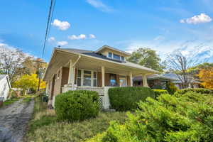 Bungalow-style home featuring covered porch, brick siding, and a shingled roof