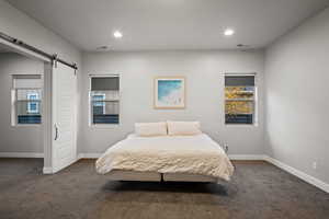 Bedroom featuring dark carpet, a barn door, multiple windows, and recessed lighting