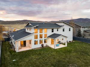 Back of house at dusk with a patio area, a shingled roof, and a mountain view