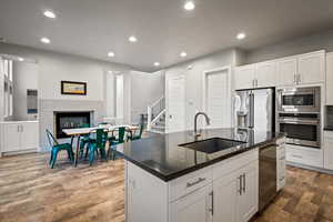 Kitchen featuring recessed lighting, appliances with stainless steel finishes, dark stone countertops, dark wood-style floors, and a center island with sink