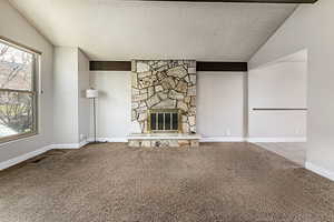 Unfurnished living room with a textured ceiling, lofted ceiling, a fireplace, and carpet floors