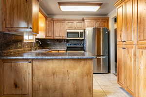 Kitchen with appliances with stainless steel finishes, backsplash, dark countertops, light tile patterned floors, and a peninsula
