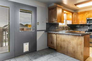 Kitchen featuring tasteful backsplash, stainless steel appliances, a peninsula, dark countertops, and brown cabinets