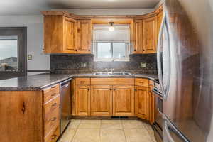 Kitchen with stainless steel appliances, a peninsula, brown cabinets, backsplash, and dark countertops