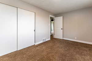 Unfurnished bedroom featuring dark carpet, a textured ceiling, and a closet