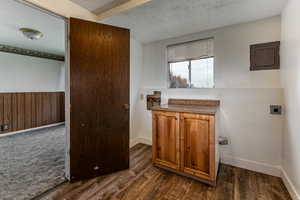 Laundry area featuring a textured ceiling, electric panel, wooden walls, a wainscoted wall, and hookup for an electric dryer