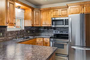Kitchen with stainless steel appliances, dark countertops, tasteful backsplash, and brown cabinets