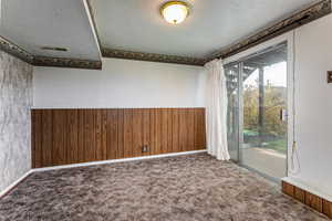 Spare room featuring wooden walls, a wainscoted wall, dark colored carpet, and a textured ceiling