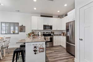 Kitchen with light stone counters, stainless steel appliances, white cabinetry, a breakfast bar, and recessed lighting