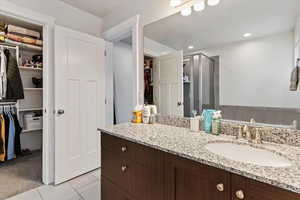 Master bathroom with a walk in closet, light tile patterned floors, vanity, a stall shower, and recessed lighting