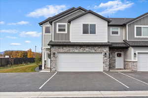 Craftsman inspired home featuring board and batten siding, stone siding, asphalt driveway, and a shingled roof