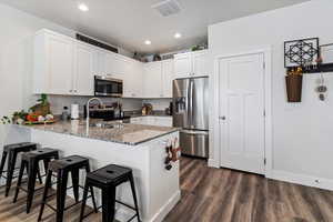 Kitchen with dark stone counters, appliances with stainless steel finishes, white cabinetry, a peninsula, and dark wood-style floors