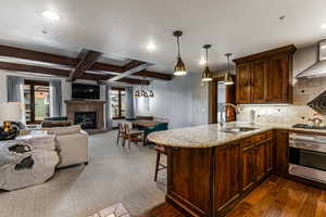 Kitchen featuring beam ceiling, light stone counters, a peninsula, hanging light fixtures, and a breakfast bar