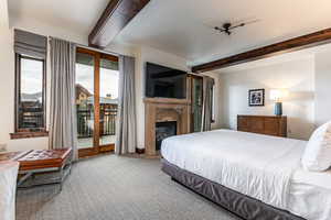 Primary bedroom featuring beamed ceiling, a glass covered fireplace, and access to outside