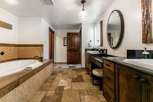 Primary Bathroom with a bath, stone tile flooring, two vanities, and a textured ceiling