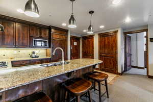 Kitchen featuring a kitchen breakfast bar, light stone countertops, dark brown cabinets, tasteful backsplash, and recessed lighting