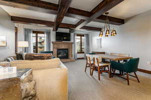 Living room featuring beam ceiling, light colored carpet, a glass covered fireplace, and coffered ceiling