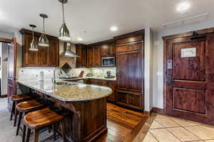 Kitchen featuring a peninsula, light stone counters, dark brown cabinets, backsplash, and recessed lighting